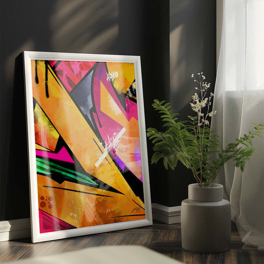 Three abstract paintings in yellow, pink, black, and blue colors with text elements hanging on the wall above a white bed with gray throw blanket and wooden nightstand with potted plant in a modern bedroom. Artwork by Kali Nuevo.