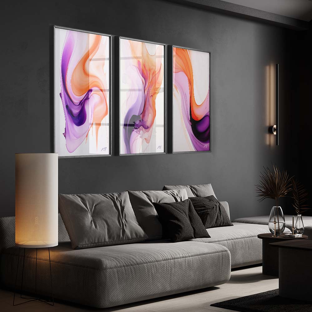 A triptych of colorful and fluid abstract paintings in a living room with a gray sofa and a white floor lamp.