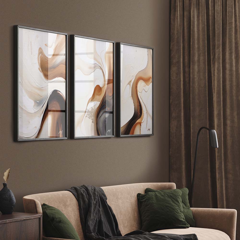 A triptych of abstract art with brown, beige, black fluid lines and shapes on a wall above a beige sofa with green pillows and a black blanket.