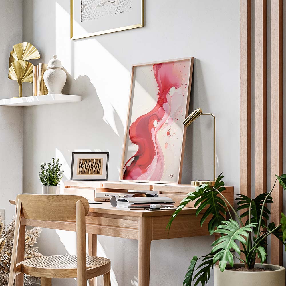 A large pink and white abstract painting in a gold frame on a shelf above a desk with a plant and books.