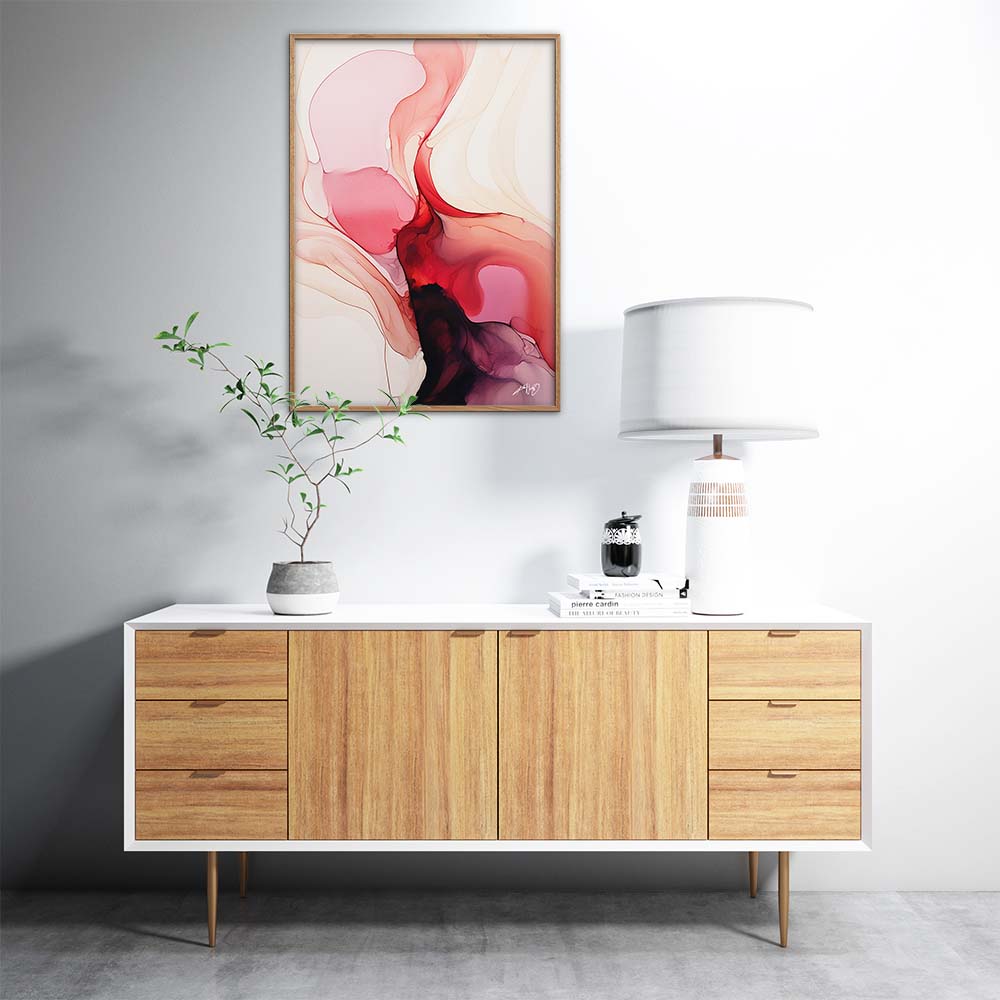 A red and pink abstract painting with white and orange accents on a white wall above a wooden stand with a lamp and a plant.