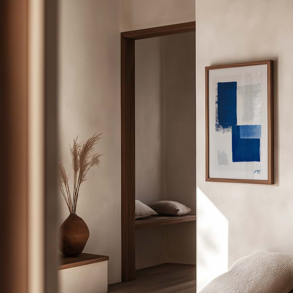 Kunstplakat med geometriske blå felter, indrammet i egetræ og vist i et lyst, skandinavisk interiør. Design af Kali Nuevo.