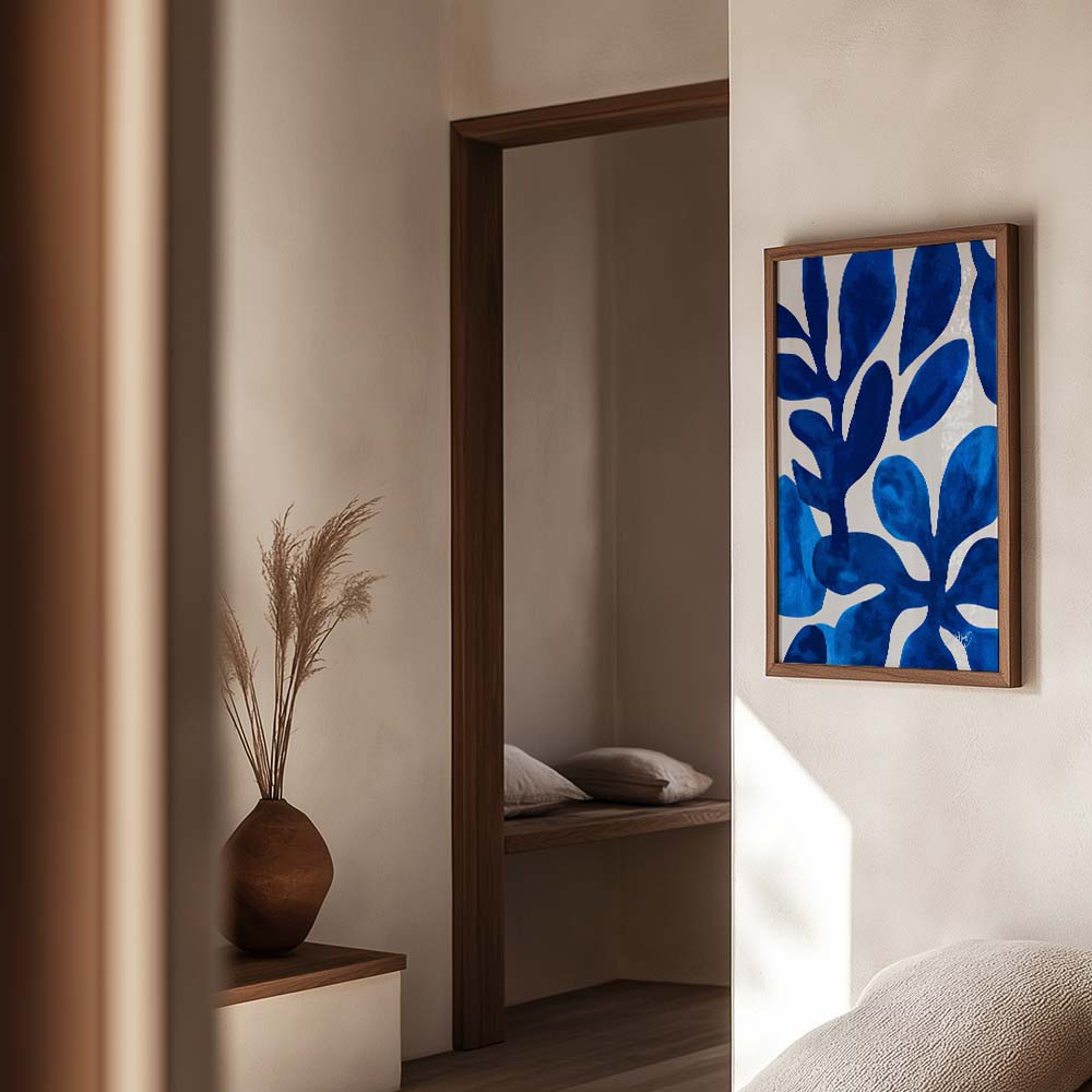 Kunstplakat med blå blomsterformer i abstrakt stil, indrammet i egetræ og vist i en varm og moderne boligindretning. Design af Kali Nuevo.