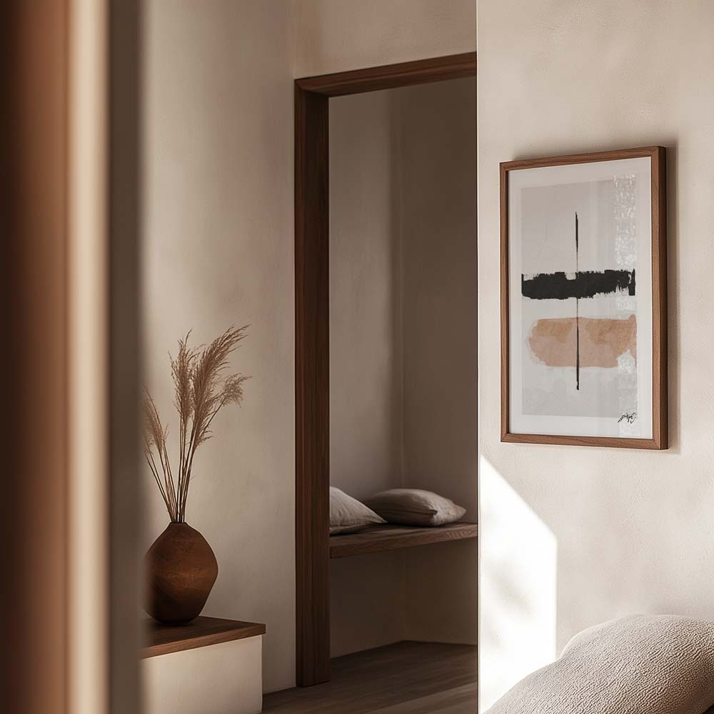 Kunstplakat med krydsende penselstrøg i sort og beige, indrammet i egetræ og vist i et roligt, naturligt interiør. Design af Kali Nuevo.