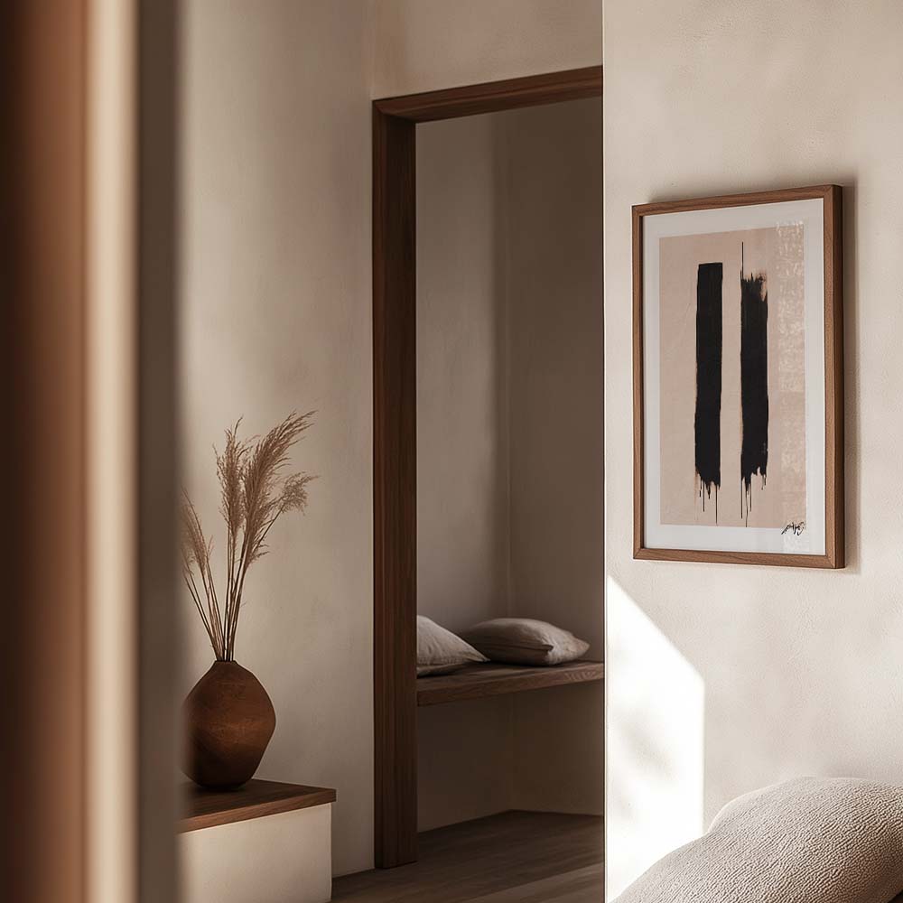 Kunstplakat med to sorte penselstrøg på beige baggrund, indrammet i egetræ og vist i et blødt og naturligt interiør. Design af Kali Nuevo.