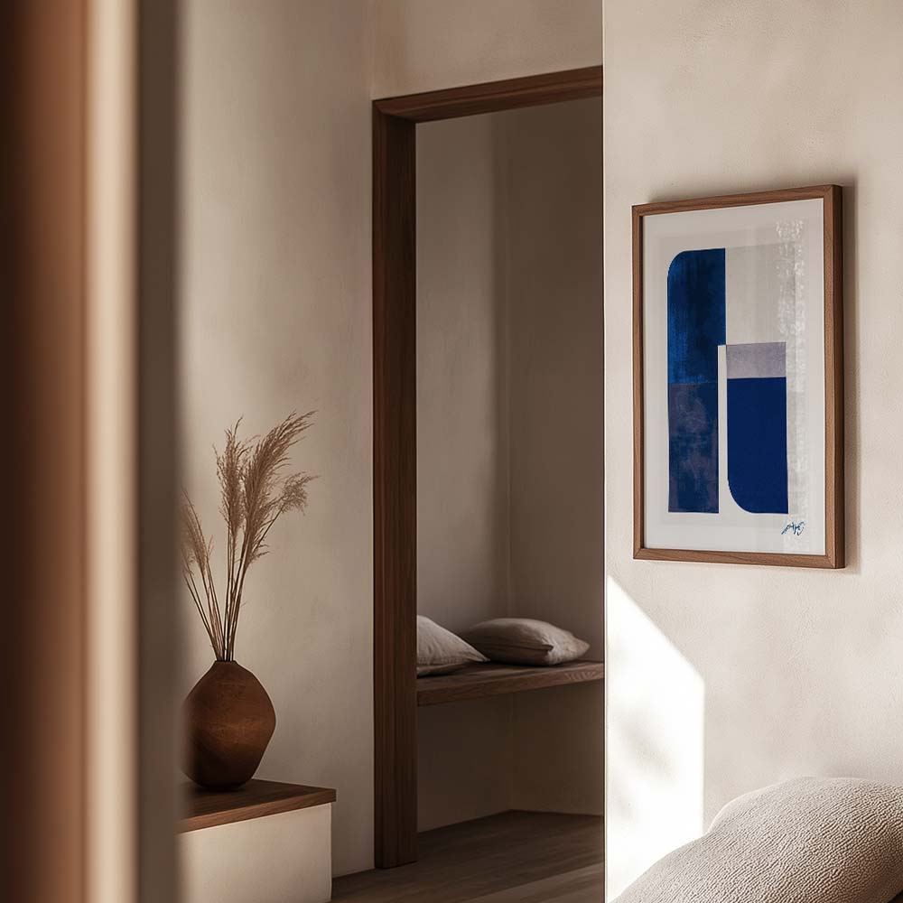 Mockup af moderne blå og grå kunstplakat i egetræsramme, vist i varm og stilren stue. Design af Kali Nuevo.