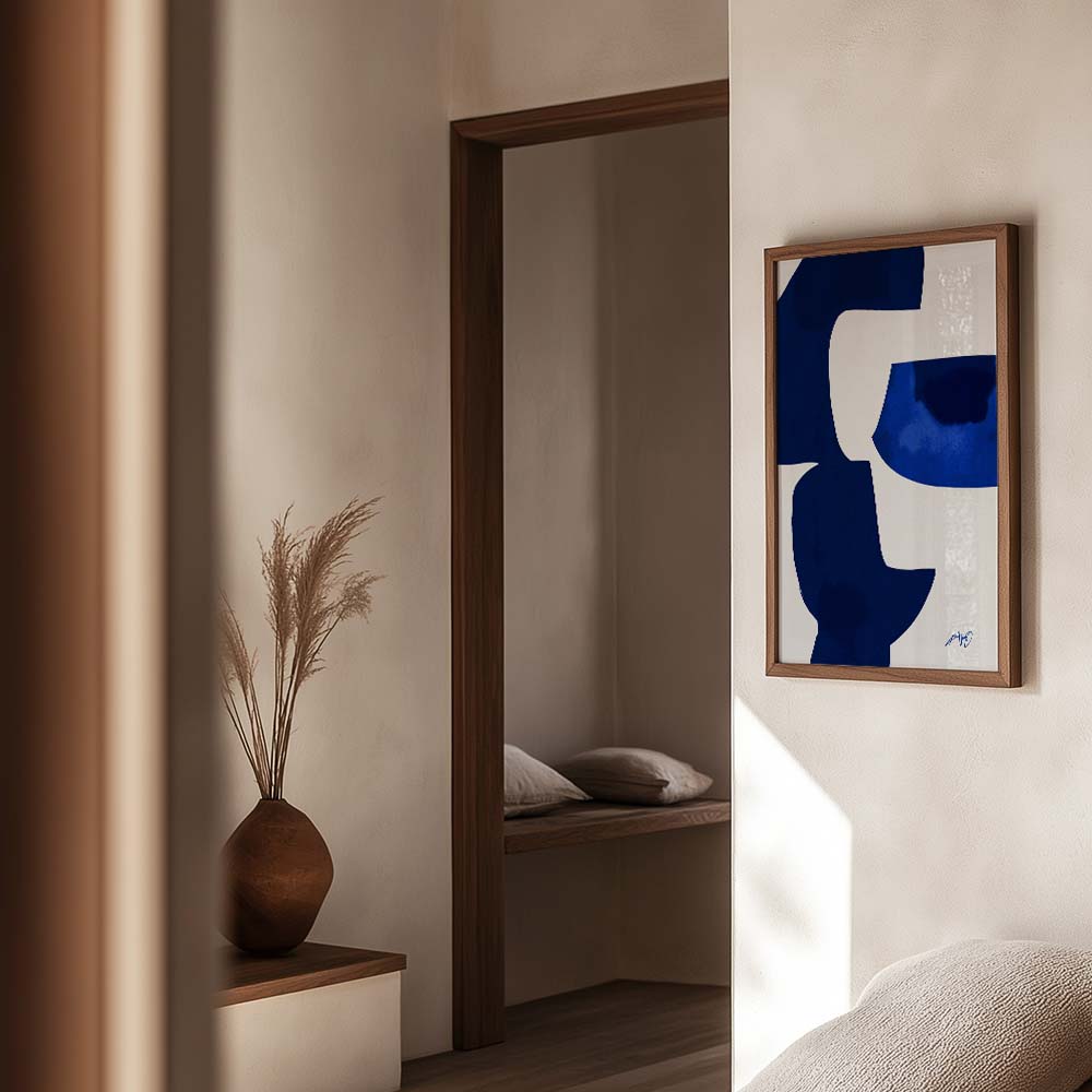 Kunstplakat i kongeblå nuancer med abstrakte former, indrammet i egetræ og vist i et elegant, lyst interiør. Design af Kali Nuevo.