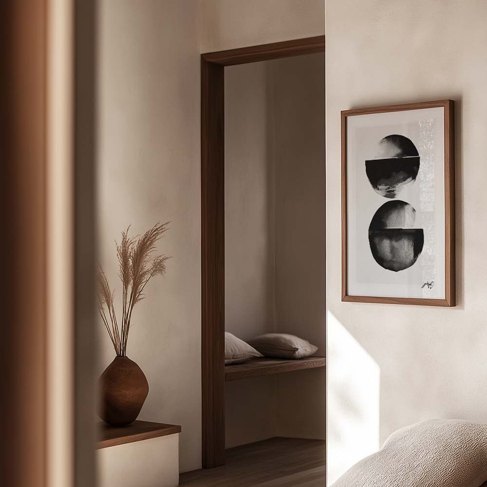 Sort-hvid kunstplakat med to cirkelformede motiver, indrammet i egetræ og vist i en varm, minimalistisk boligindretning. Design af Kali Nuevo.