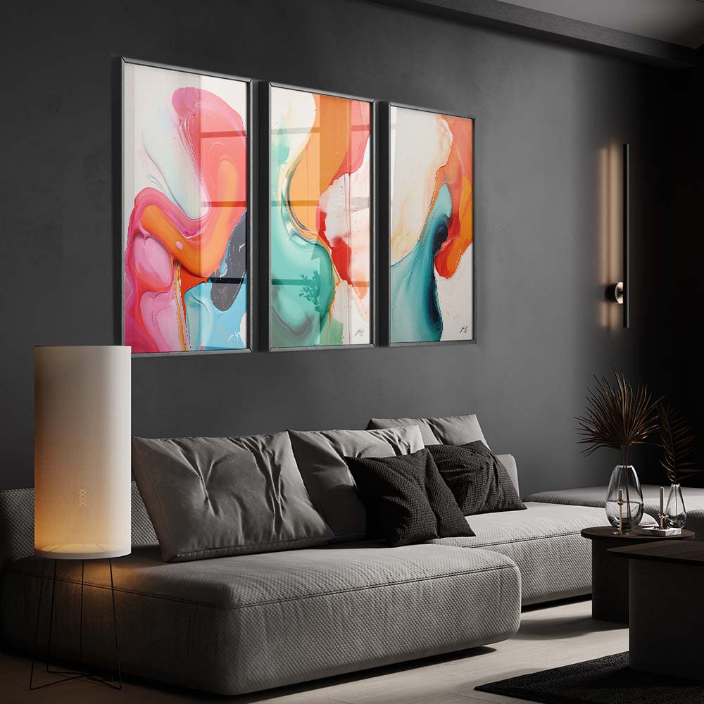 A triptych of colorful and fluid abstract paintings in a living room with a gray sofa and a white floor lamp.