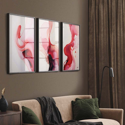 A triptych of pink, red, and black abstract paintings in a living room with a beige sofa and a black floor lamp.