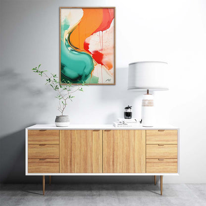 An orange, red and green abstract painting on a white wall above a wooden sideboard with a lamp, a plant, and a candle.